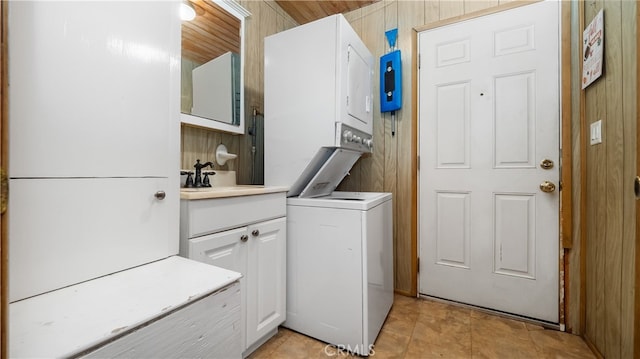 washroom with cabinets, stacked washer and dryer, wood walls, and sink