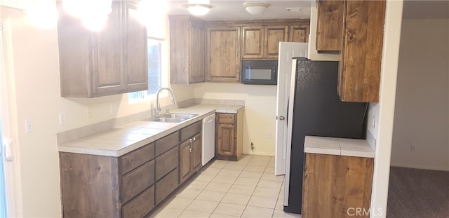 kitchen with black appliances, tile countertops, light tile patterned floors, and sink