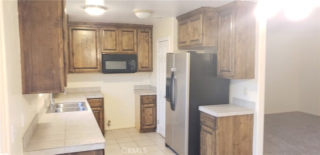 kitchen with sink, tile countertops, stainless steel fridge, and light tile patterned floors