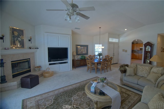 carpeted living room featuring ceiling fan with notable chandelier, lofted ceiling, and a tiled fireplace