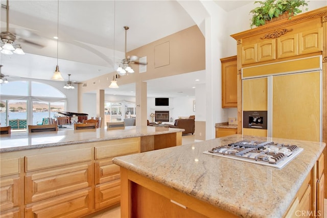 kitchen with a ceiling fan, a center island, a fireplace, white gas cooktop, and light stone countertops