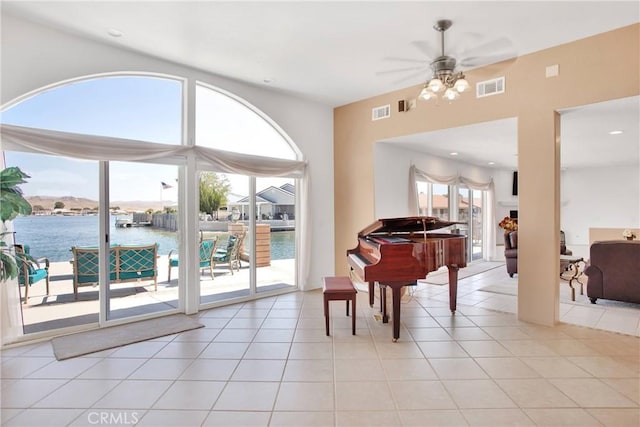 living area with light tile patterned floors, visible vents, a ceiling fan, and a water view