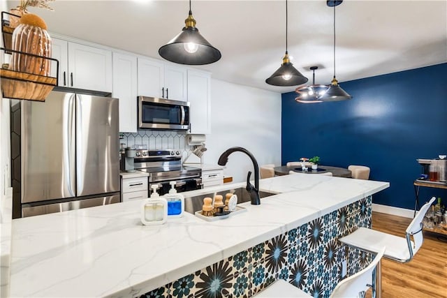 kitchen with pendant lighting, light hardwood / wood-style flooring, light stone countertops, white cabinetry, and stainless steel appliances