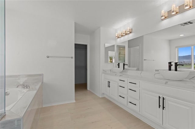 bathroom with hardwood / wood-style floors, vanity, and a relaxing tiled tub