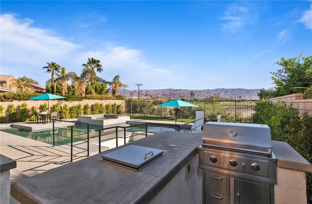 view of patio featuring a fenced in pool, grilling area, a mountain view, and exterior kitchen