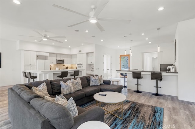 living room featuring light hardwood / wood-style flooring, ceiling fan, and sink