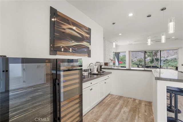 kitchen with kitchen peninsula, sink, pendant lighting, white cabinets, and light hardwood / wood-style floors