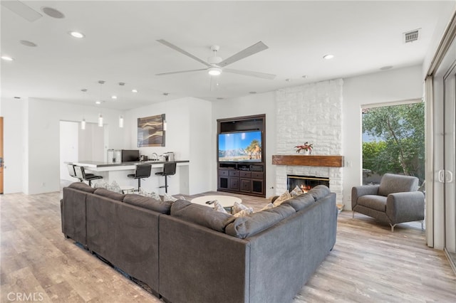 living room with ceiling fan, a fireplace, and light hardwood / wood-style flooring