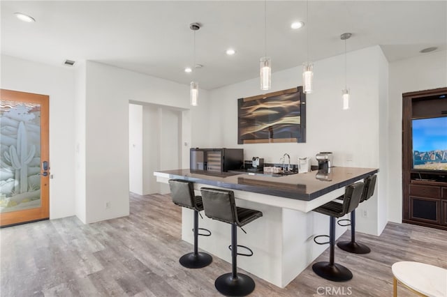 kitchen with a kitchen bar, kitchen peninsula, hanging light fixtures, and light hardwood / wood-style flooring