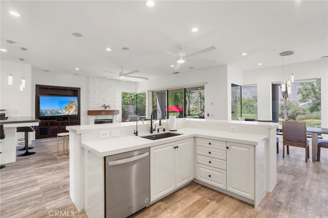 kitchen featuring white cabinetry, sink, hanging light fixtures, stainless steel dishwasher, and light wood-type flooring