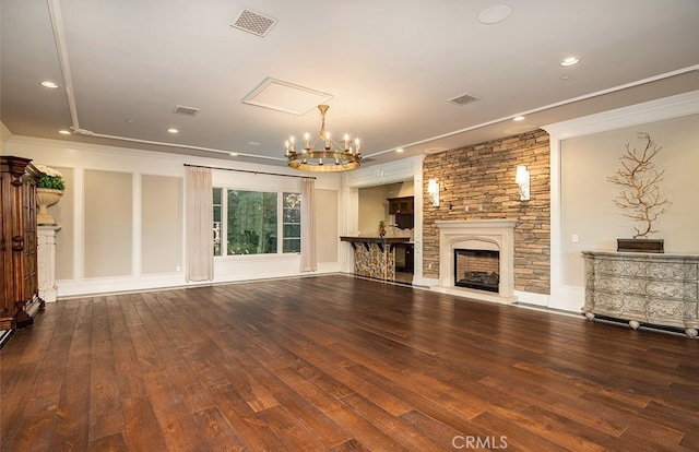 unfurnished living room with crown molding, a stone fireplace, wood-type flooring, and an inviting chandelier