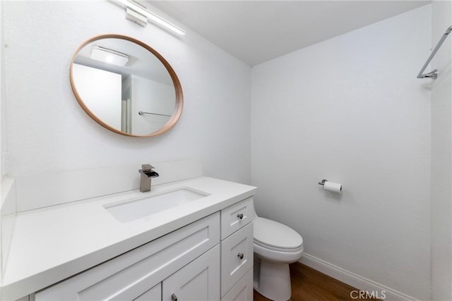 bathroom featuring baseboards, wood finished floors, toilet, and vanity