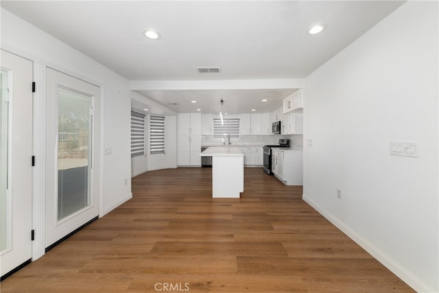 kitchen featuring white cabinets, pendant lighting, a kitchen island, wood-type flooring, and appliances with stainless steel finishes