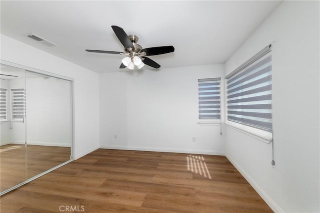 unfurnished bedroom featuring baseboards, visible vents, a ceiling fan, a closet, and wood finished floors