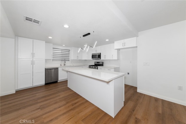 kitchen featuring hanging light fixtures, white cabinetry, appliances with stainless steel finishes, dark hardwood / wood-style floors, and a center island