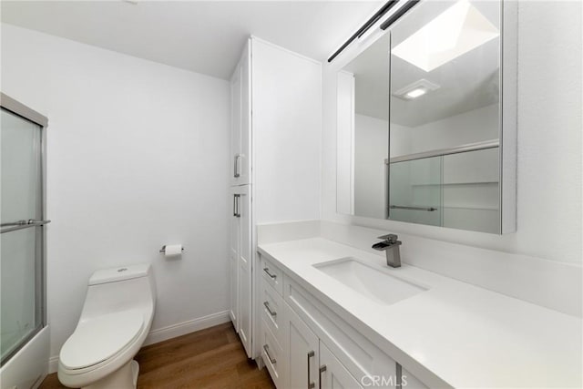 bathroom featuring baseboards, a shower with shower door, toilet, wood finished floors, and vanity