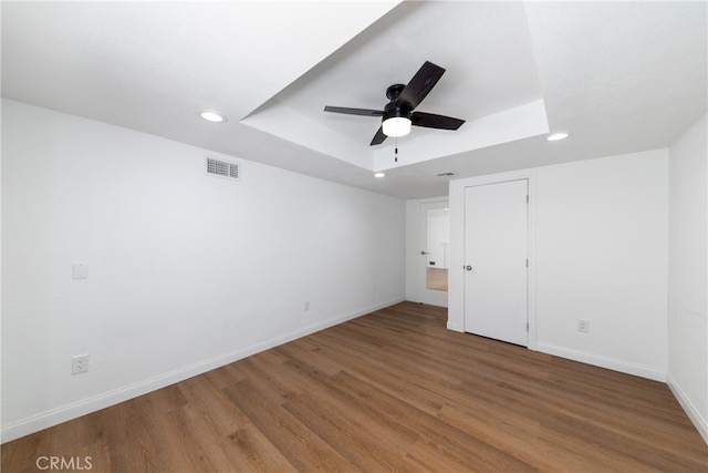 unfurnished bedroom with wood-type flooring, a tray ceiling, and ceiling fan