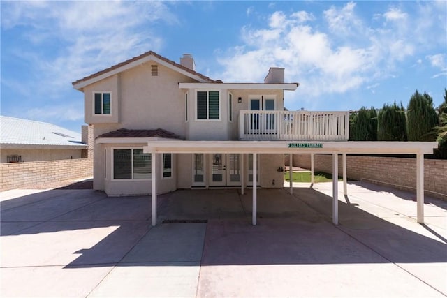 rear view of property featuring a balcony, a tiled roof, stucco siding, and fence
