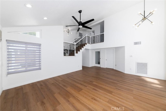 unfurnished living room featuring stairs, visible vents, ceiling fan with notable chandelier, and wood finished floors