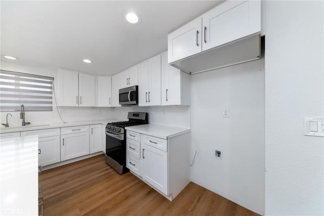 kitchen featuring light countertops, wood finished floors, appliances with stainless steel finishes, white cabinetry, and a sink