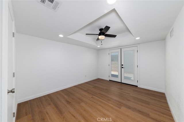 spare room featuring wood-type flooring, a tray ceiling, ceiling fan, and french doors