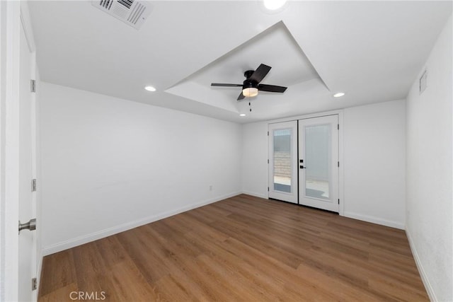 spare room featuring baseboards, visible vents, wood finished floors, and a raised ceiling