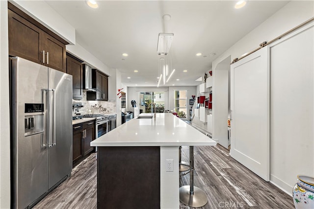 kitchen with high end appliances, a barn door, a kitchen breakfast bar, a center island with sink, and dark hardwood / wood-style flooring