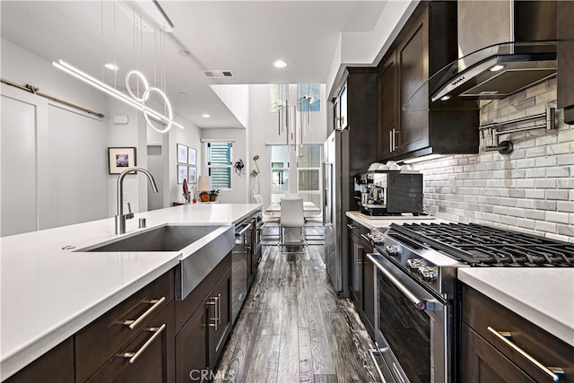 kitchen with decorative backsplash, wall chimney exhaust hood, premium appliances, dark brown cabinetry, and dark hardwood / wood-style floors