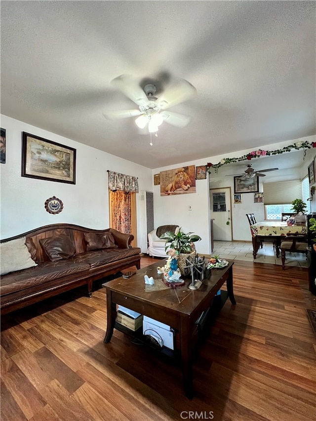 living room with a textured ceiling, ceiling fan, and hardwood / wood-style flooring