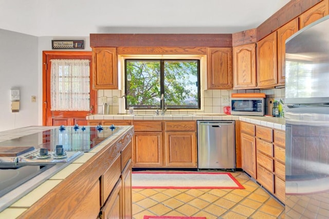 kitchen featuring decorative backsplash, appliances with stainless steel finishes, sink, light tile patterned floors, and tile counters