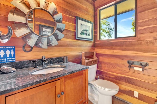 bathroom with vanity, wood walls, and toilet