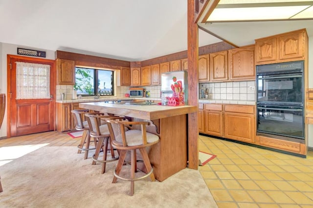 kitchen with backsplash, a kitchen breakfast bar, vaulted ceiling, appliances with stainless steel finishes, and a kitchen island