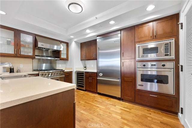 kitchen featuring light hardwood / wood-style floors, built in appliances, sink, ventilation hood, and beverage cooler