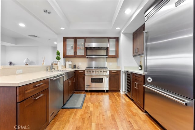 kitchen featuring wine cooler, wall chimney exhaust hood, high end appliances, a tray ceiling, and light hardwood / wood-style flooring