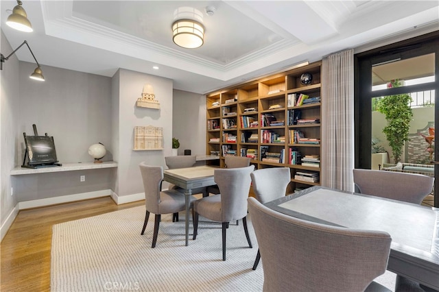 dining room featuring light wood-type flooring, crown molding, a tray ceiling, and built in desk