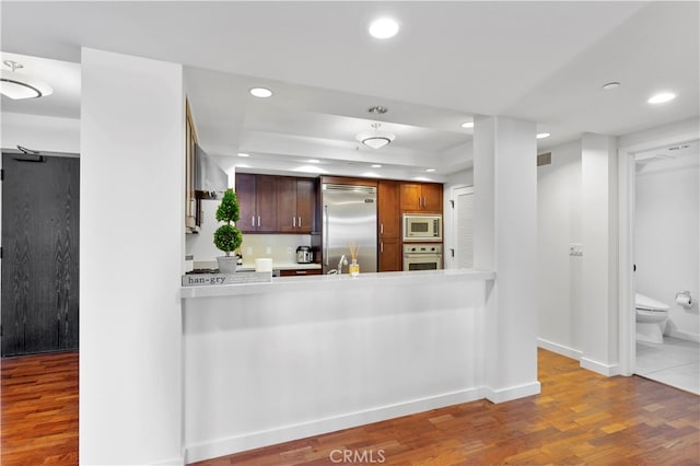 kitchen featuring a raised ceiling, kitchen peninsula, built in appliances, hardwood / wood-style floors, and sink