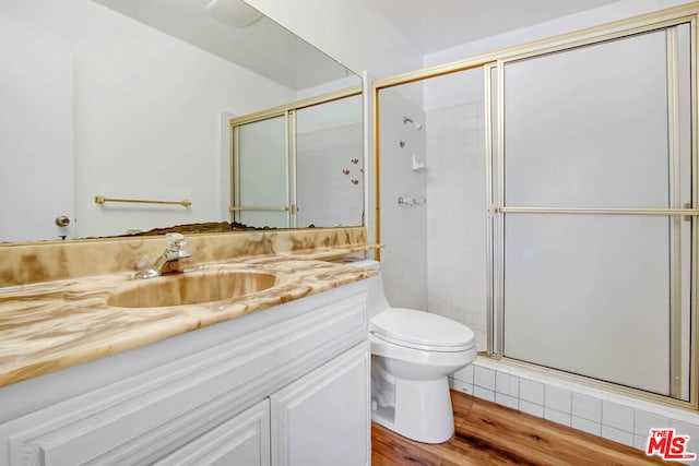 bathroom with wood-type flooring, vanity, toilet, and a shower with shower door