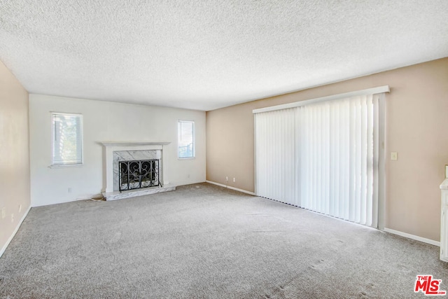 unfurnished living room featuring carpet floors, a wealth of natural light, a high end fireplace, and a textured ceiling