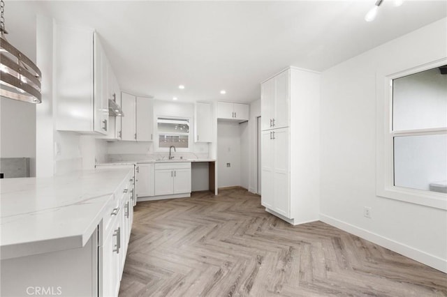 kitchen with white cabinets, light stone counters, sink, and light parquet flooring