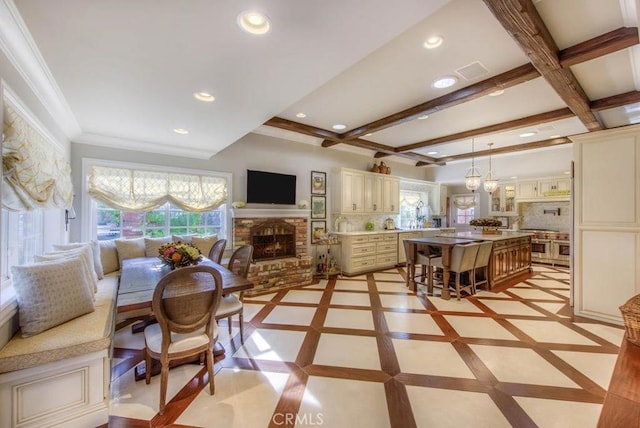 dining area featuring a brick fireplace, a chandelier, and beam ceiling