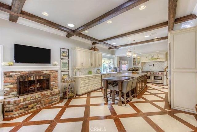 kitchen with double oven range, a kitchen bar, a kitchen island, a brick fireplace, and cream cabinetry