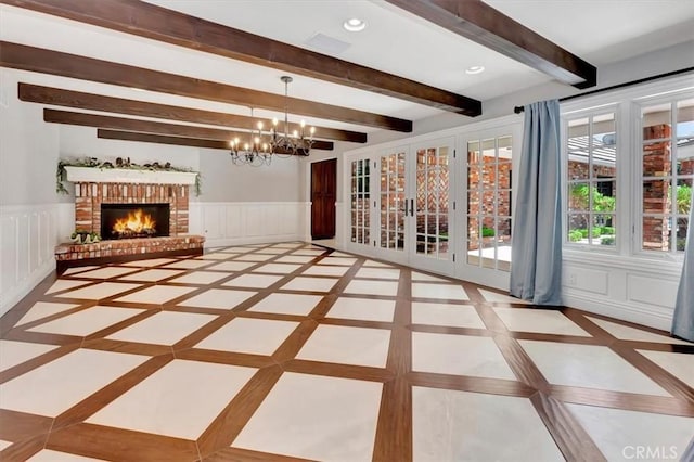 interior space with beamed ceiling, a brick fireplace, and a chandelier