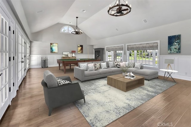 living room with vaulted ceiling, billiards, french doors, hardwood / wood-style floors, and an inviting chandelier