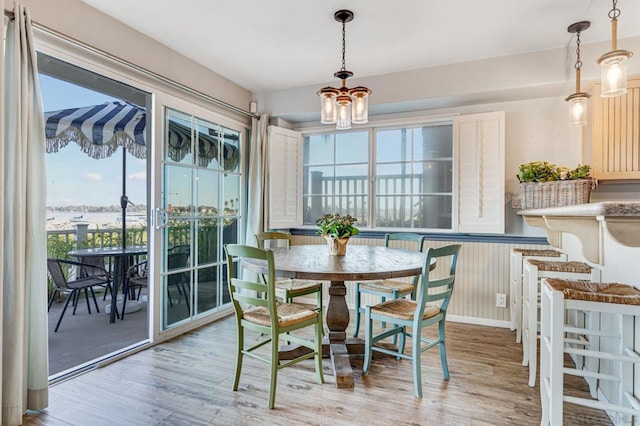 dining area with light wood-type flooring, a healthy amount of sunlight, and a notable chandelier