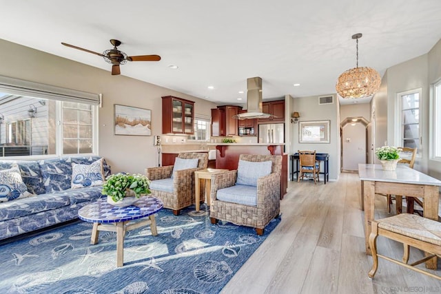 living room with ceiling fan with notable chandelier, light hardwood / wood-style floors, sink, and a wealth of natural light