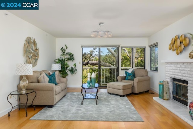 living room featuring a brick fireplace, light hardwood / wood-style floors, and a notable chandelier