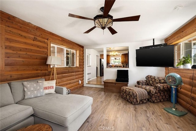 living room featuring ceiling fan with notable chandelier, wooden walls, and light hardwood / wood-style flooring