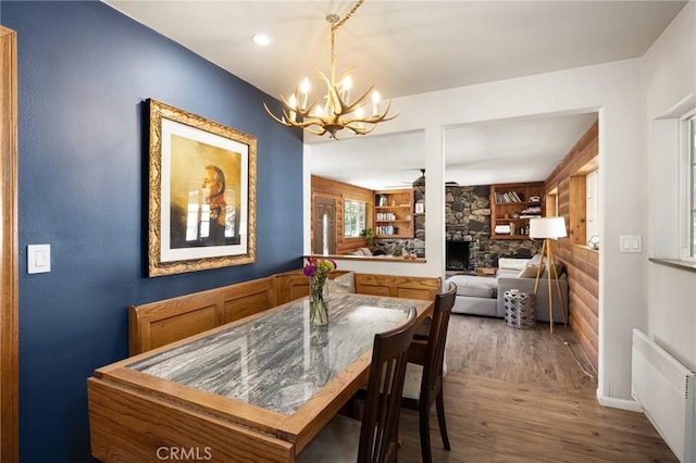 dining room with wood-type flooring, ceiling fan with notable chandelier, a stone fireplace, and radiator