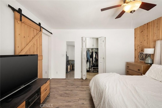 bedroom with ceiling fan, dark wood-type flooring, a barn door, a closet, and wood walls