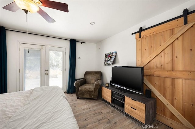 bedroom featuring ceiling fan, french doors, a barn door, hardwood / wood-style floors, and access to outside